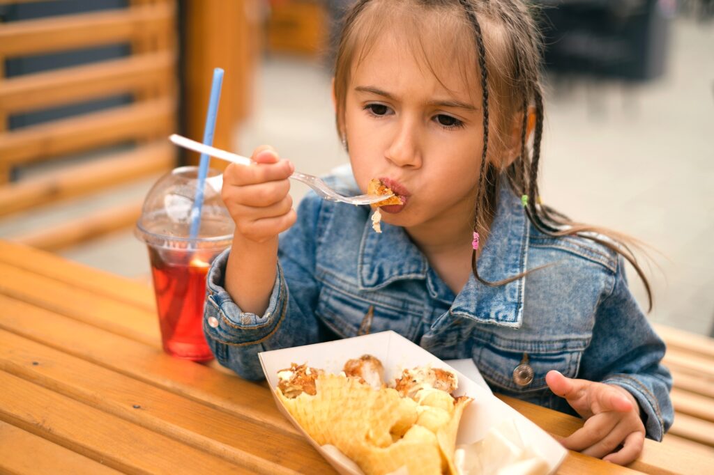 A child bites hard food while sitting at a table in a city cafe outdoors