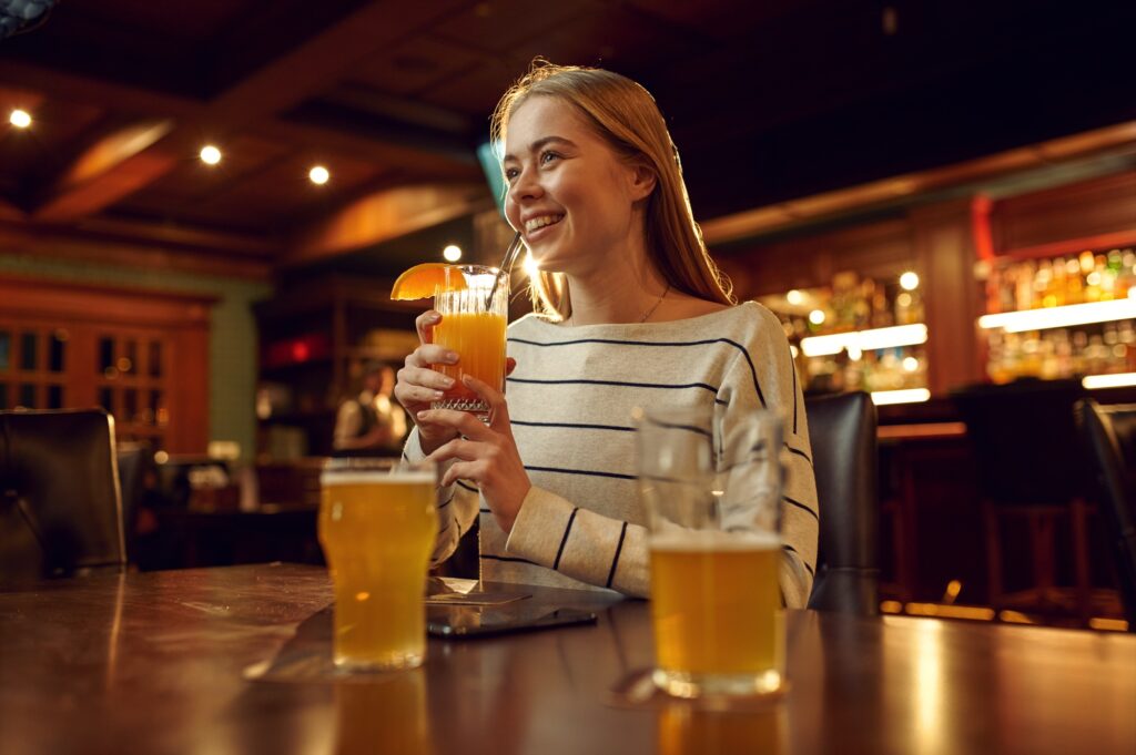 Cheerful young woman drinks coctail in bar