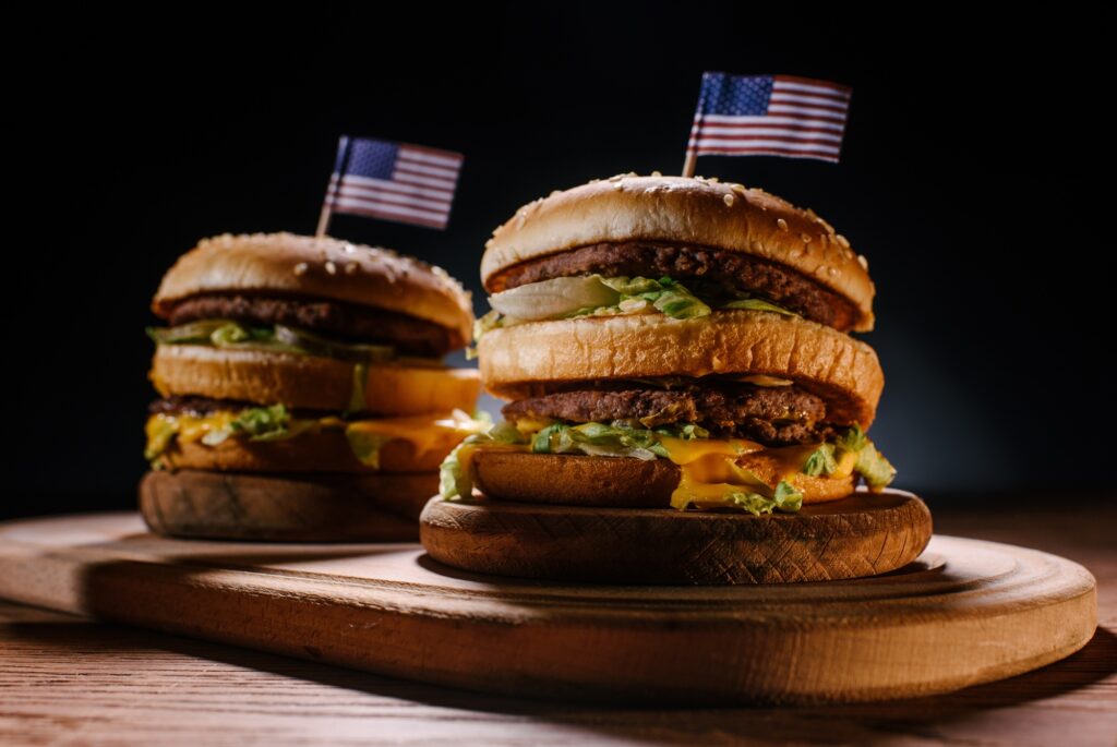 close-up shot of delicious burgers with usa flag pins on wooden cutting board on black