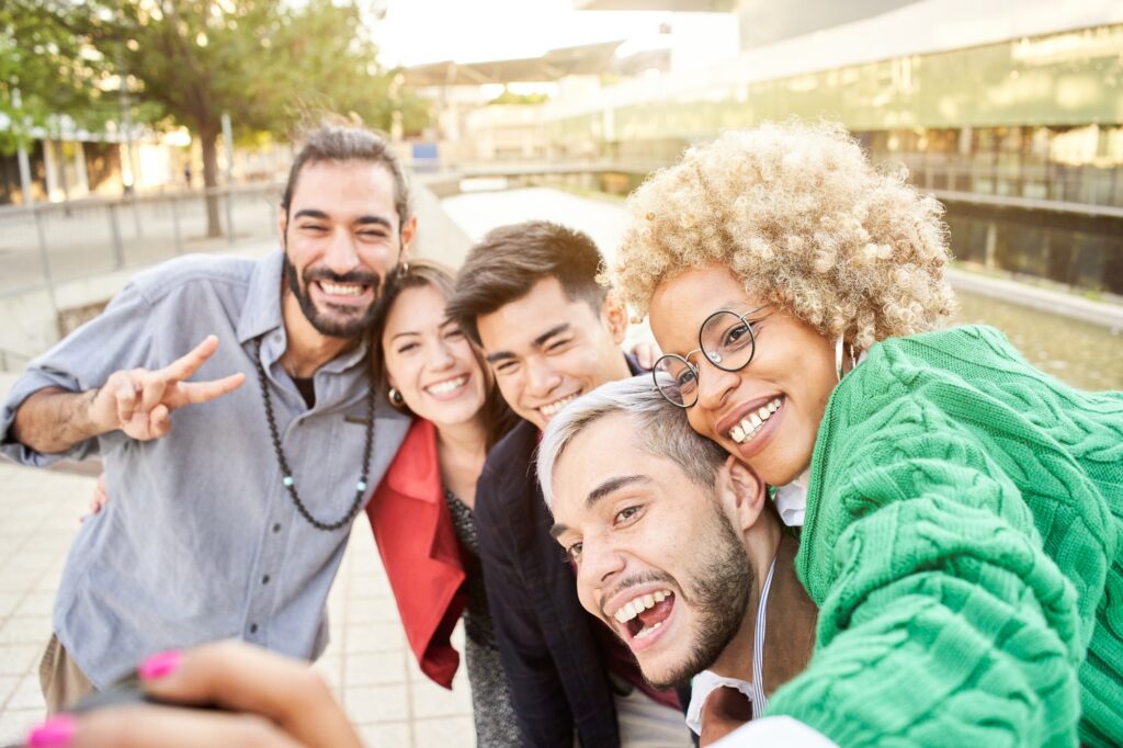 Group of cheerful friends taking smiling selfies outdoors